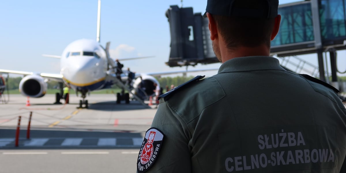 Funkcjonariusz służby celno-skarbowej w mundurze, w tle samolot