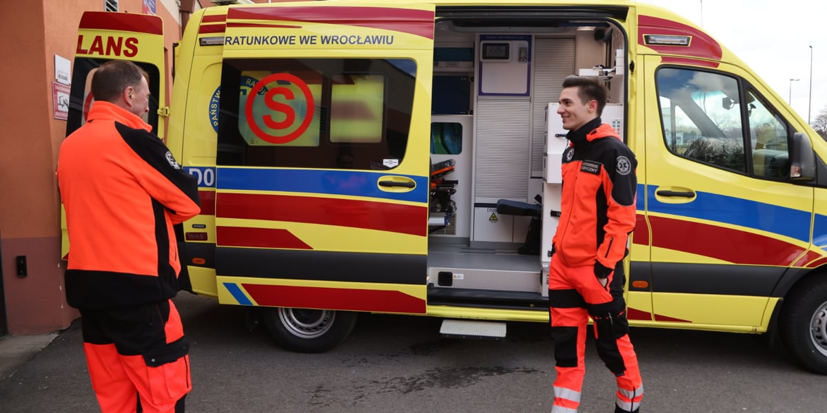 Ratownicy medyczni w służbowych strojach przed nową, żółtą karetką