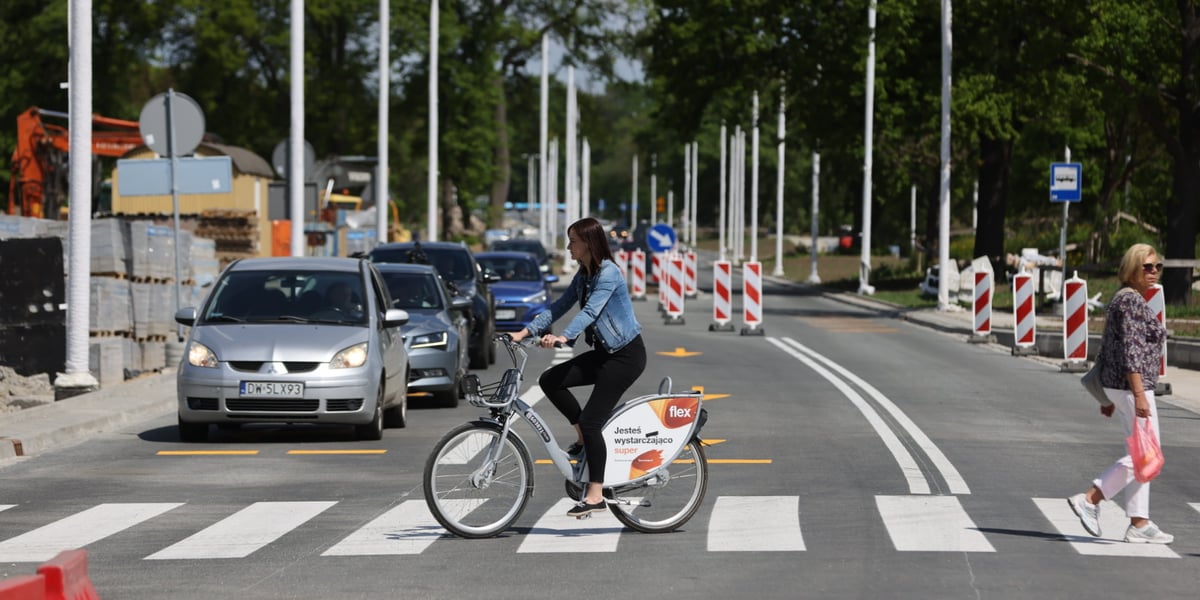 Rowerzystka przejeżdżająca przez pasy i stojące samochody na otwartym odcinku AWW