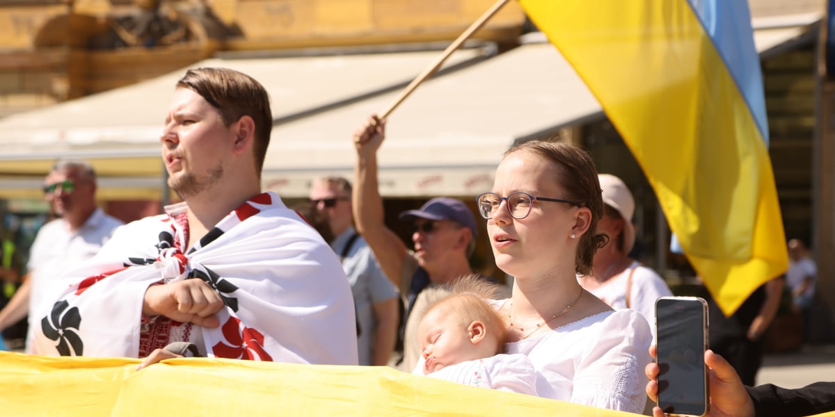 Mężczyzna i kobieta z małym dzieckiem na ręku. W tle widać ukraińską flagę