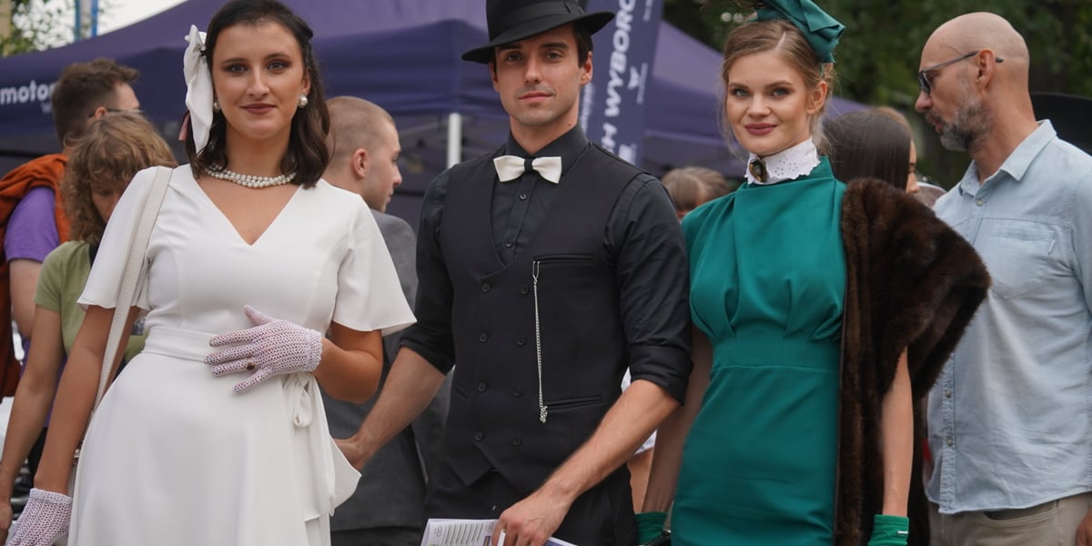 Tysiące widzów na Wielkiej Wrocławskiej na torze wyścigów konnych Partynice. Na zdjęciu dwie młode kobiety i młody mężczyzna w eleganckich strojach.