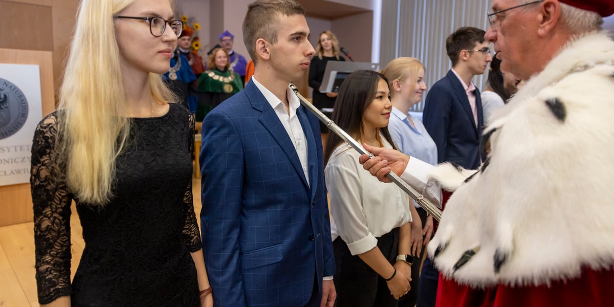 Rektor Uniwersytetu Przyrodniczego prof. Jarosław Bosy pasuje berłem nowego studenta uczelni. Obok studenta, po obu stronach, stoją studentki