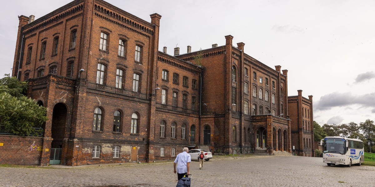 Mężczyzna z bagażem na kółkach idący w stronę budynku dworca Nadodrze