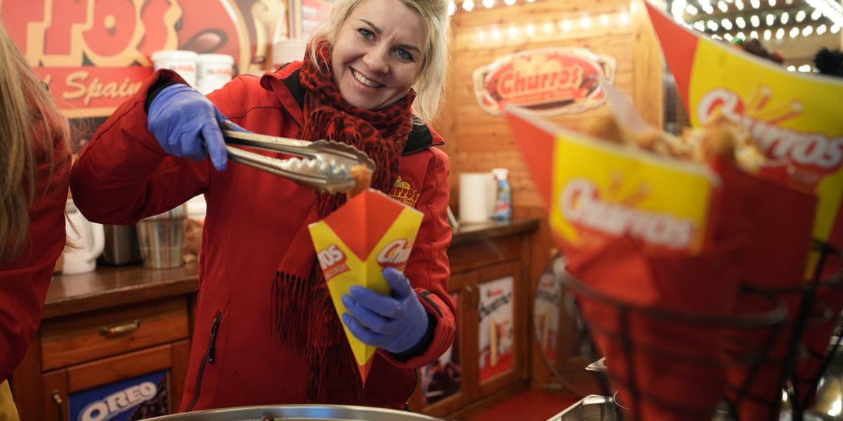 Kobieta w czerwonym płaszczu nakłada churros przy jednym ze stoisk Jarmarku Bożonarodzeniowego
