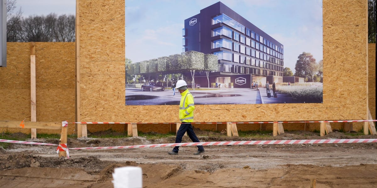 Budowlaniec w białym kasku spacerujący na tle wizualizacji hotelu