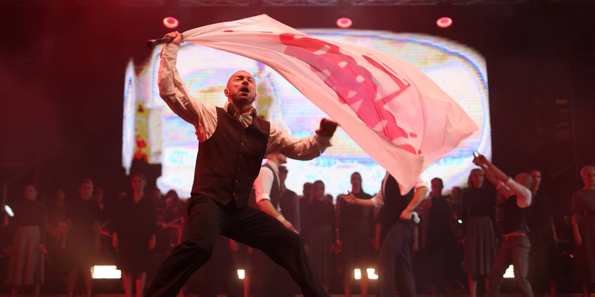Spektakl "75, czyli powojenna historia Wrocławia". Mężczyzna na scenie z białą flagą z napisem "Solidarność"