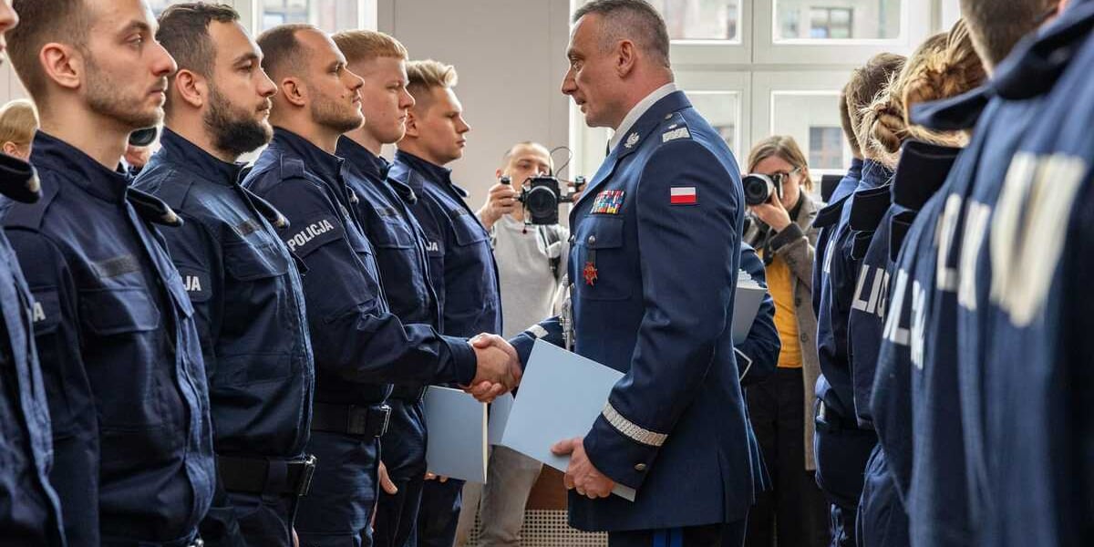 Ślubowanie nowych policjantów. Na zdjęciu mężczyzna w policyjnym mundurze gratuluje młodym policjantom stojącym w szeregu