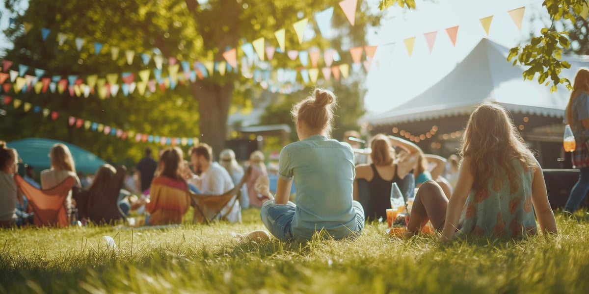 Na zdjęciu dwie młode kobiety siedzą na trawie podczas koncertu plenerowego