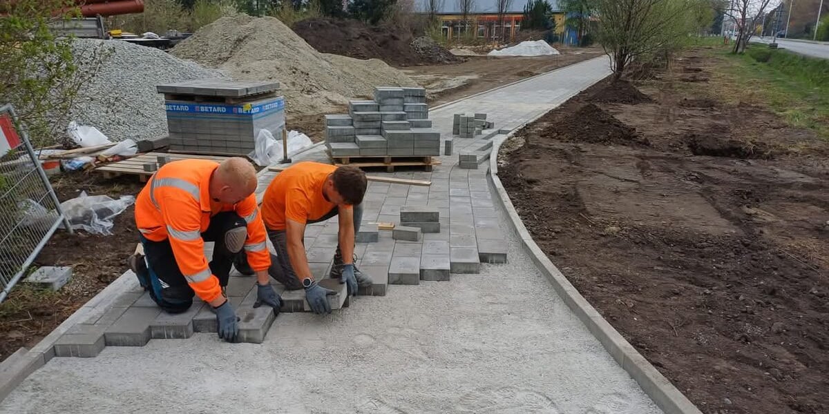 Dwóch mężczyzn układających nawierzchnię chodnika przy ulicy Kurpiów.