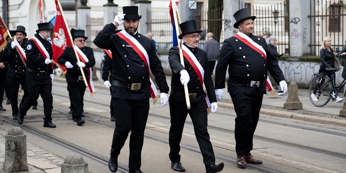 Parada kominiarzy we Wrocławiu. Na zdjęciu poczet sztandarowy organizacji kominiarskiej, trzech mężczyzn w czarnych strojach i w kapeluszach.