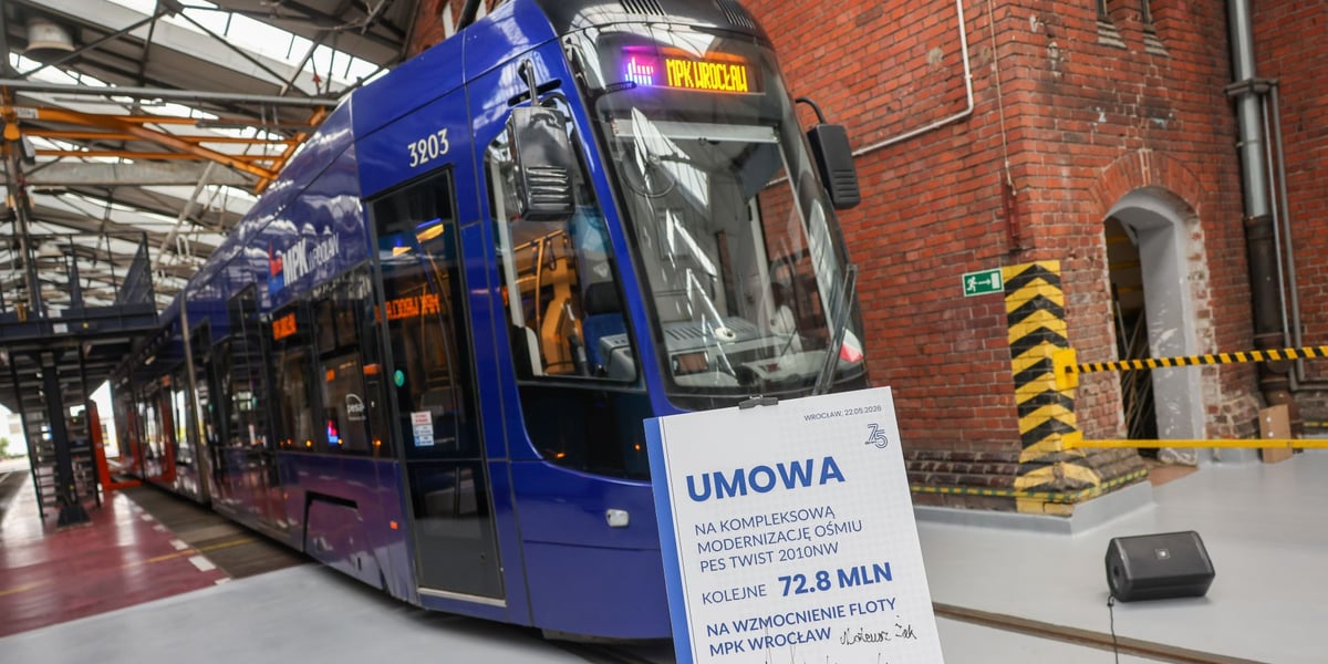 Tramwaj Pesa 2010NW na zajezdni Gaj, a przed nim tablica symbolizująca umowę na modernizację tych pojazdów