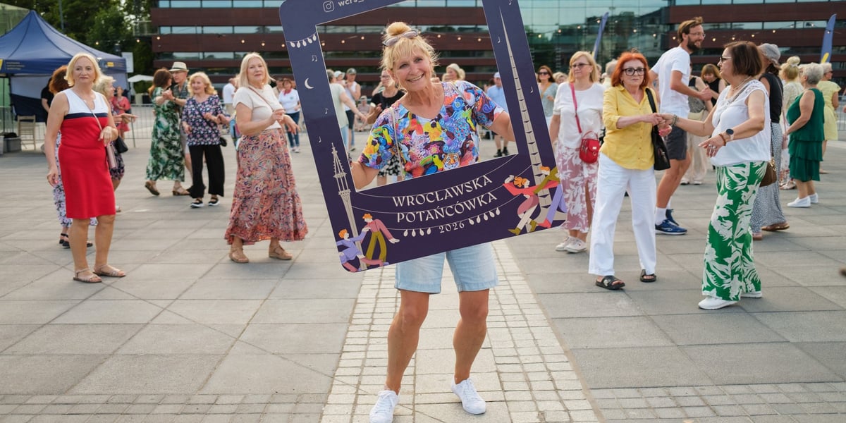 Uśmiechnięta kobieta tańczy trzymając planszę z napisem 2026 / 19.06.2026 r.