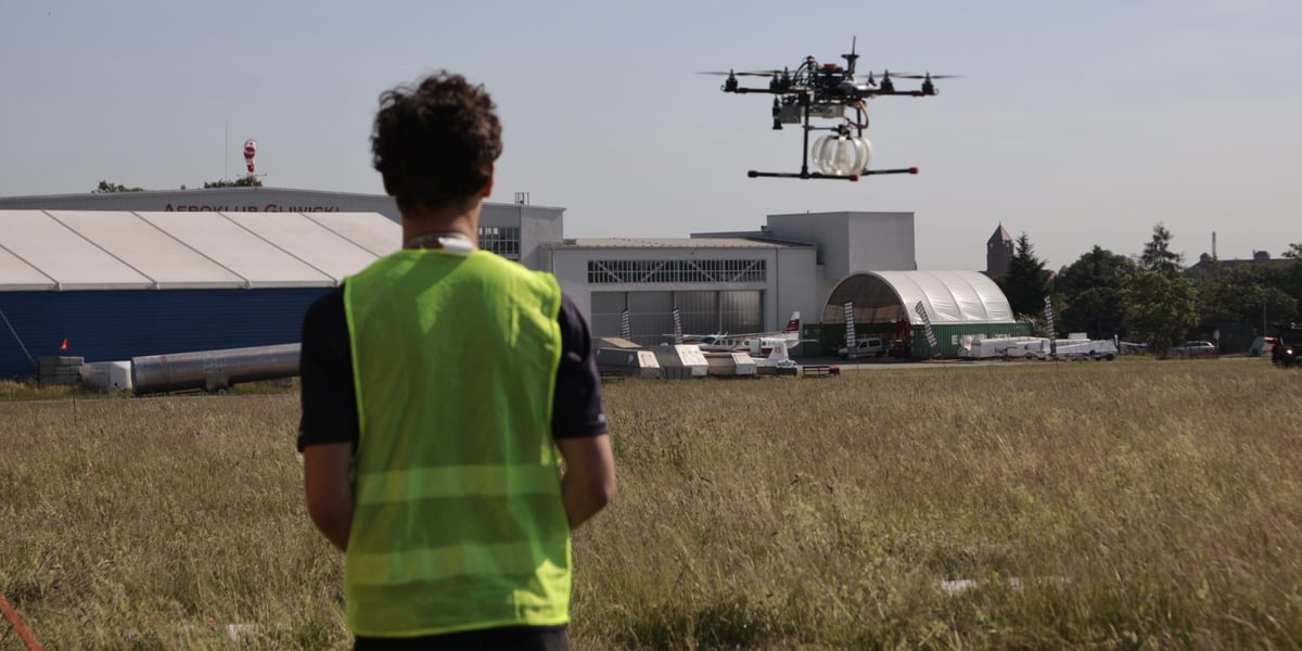 Mężczyzna w odblaskowej kamizelce steruje dronem.