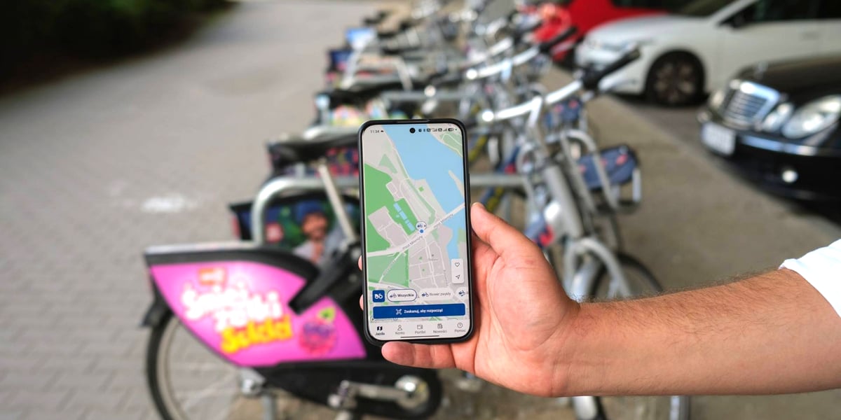 osoba pokazuje na ekranie telefonu mapę z lokalizacją stacji przy ul. Wejherowskiej, w tle zaparkowane rowery systemu WRM
