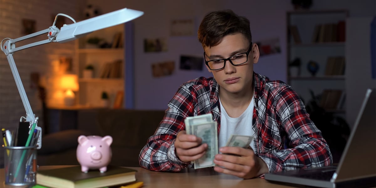 Na zdjęciu młody człowiek w okularach przelicza banknoty. Zdjęcie ilustracyjne