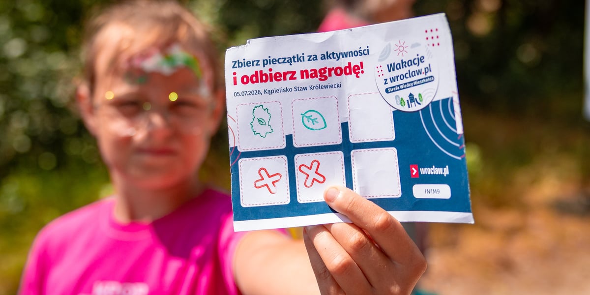 Chłopiec pokazuje kartkę służącą do zbierania pieczątek i zdobywania nagród. Zdjęcie z pikniku na Maślicach