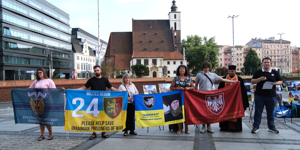 Uczestnicy wiecu pamięci jeńców wojennych i ofiar rosyjskiej agresji na Ukrainie przy fontannie na ul. Oławskiej trzymają transparenty i ukraińskie flagi - 31 lipca 2026 r.
