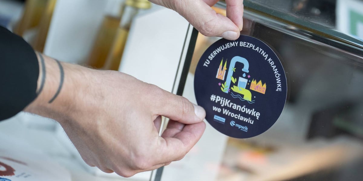 Dłonie naklejające naklejkę informującą, że w tym lokalu serwuje się kranówkę