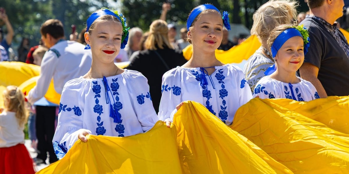 Trzy uśmiechnięte dziewczynki trzymają w rękach ukraińską flagę. Międzykulturowy piknik z okazji 35. rocznicy niepodległości Ukrainy, 22.08.2026 r. 