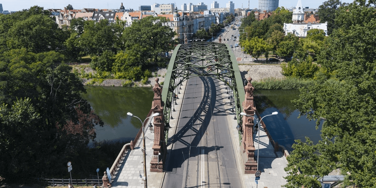 Zdjęcie z lotu ptaka pokazuje zielony, stalowy most z torami tramwajowymi nad rzeką. Przy wjazdach stoją wieżyczki, wokół rośnie dużo zieleni, a w tle widać Wrocław. Most Zwierzyniecki znalazł się na liście, ogłoszonej latem 2026 przez Zarząd Dróg i Utrzymania Miasta, programu remontów mostów. 