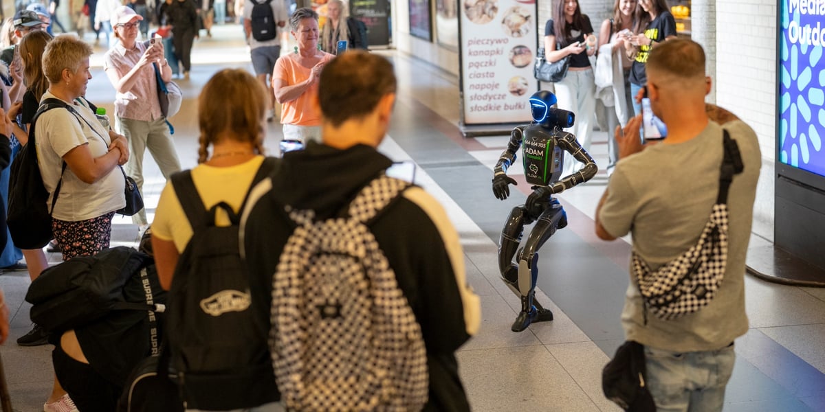 Humanoidalny robot "Adam Kowalski" tańczy przy wejściu na perony dworca Wrocław Główny. Występowi przygląda się tłum ludzi, kilkoro z nich robi zdjęcia telefonami komórkowymi.