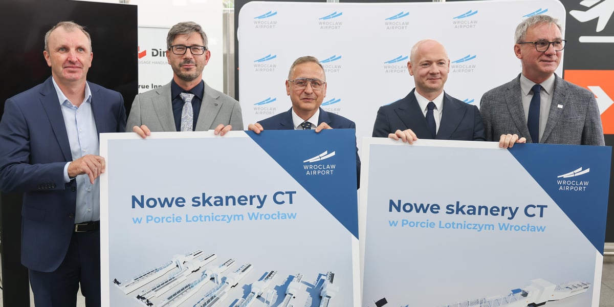 Piątka mężczyzn w garniturach trzymająca plansze z wizualizacjami linii w strefie kontroli bezpieczeństwa na lotnisku we Wrocławiu, 7 września 2026. Od lewej: Marcin Janusz (Anglosec), Błażej Nowakowski (Dimark), Cezary Pacamaj, Karol Przywara i Dariusz Kowalczk