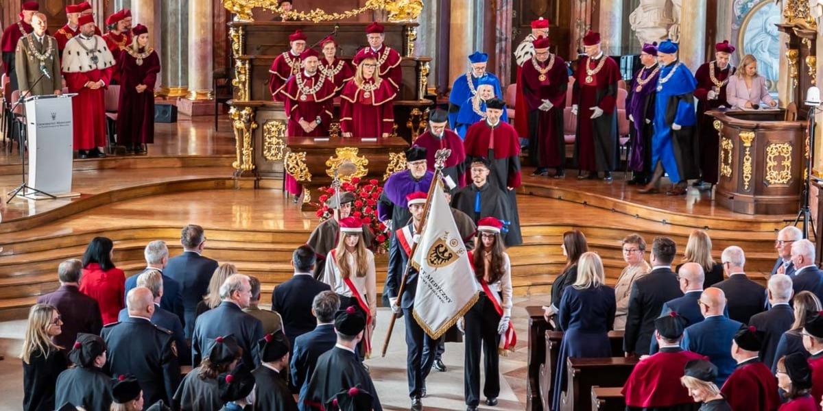 Orszak podczas uroczystości rozpoczęcia roku akademickiego prowadzony przez delegację studentów ze sztandarem uczelni, dalej idą przedstawiciele władz Uniwersytetu Medycznego w togach.