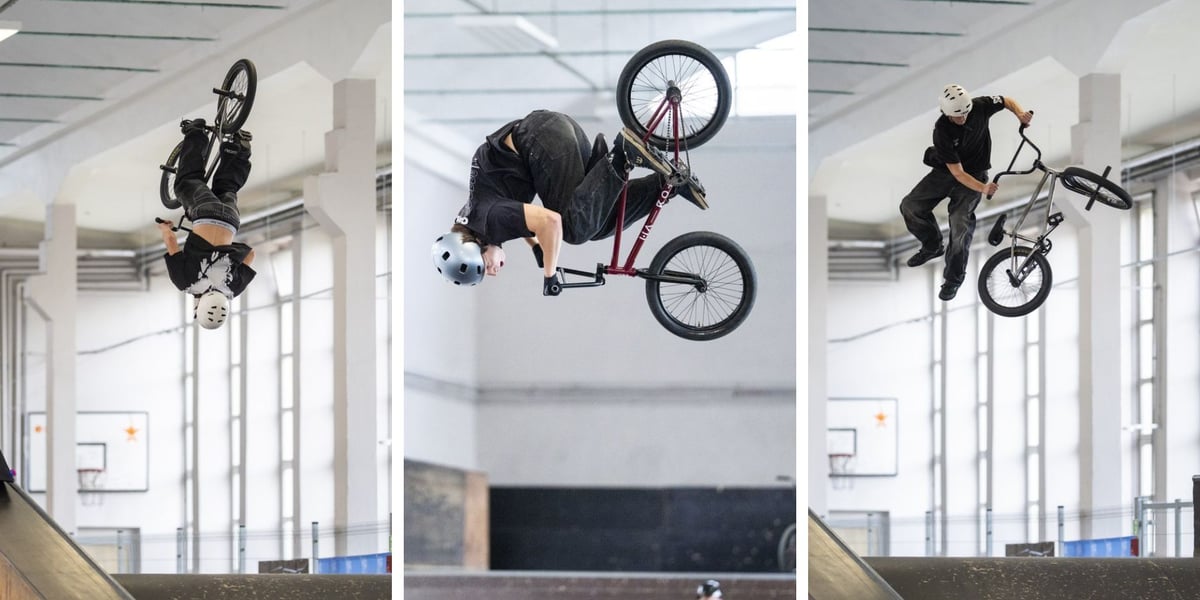Trzech zawodników w kaskach wykonuje skoki na rowerach BMX w hali skateparku, wśród nich chłopiec w niebieskiej koszulce. W sobotę, 17 października, skatepark przy ul. Legnickiej we Wrocławiu zamienił się w arenę BMX Freestyle Contest 2026.