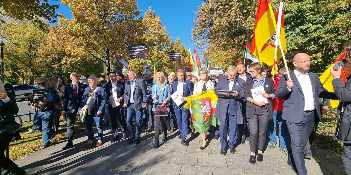 Na zdjęciu grupa samorządowców idąca chodnikiem z flagami 