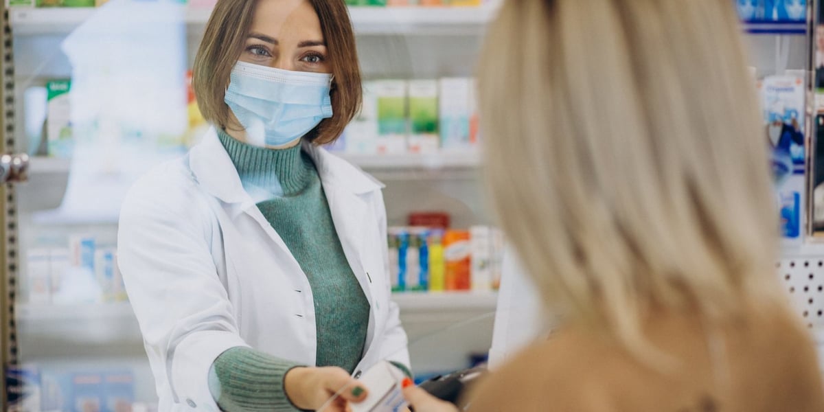 na zdjęciu farmaceutka w maseczce podaje leki odwróconej tyłem kobiecie