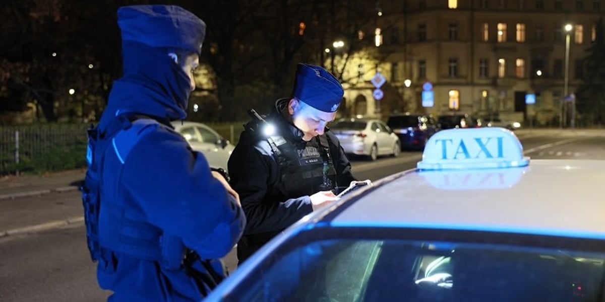 Na zdjęciu dwaj policjanci podczas kontroli dokumentów kierowcy taksówki