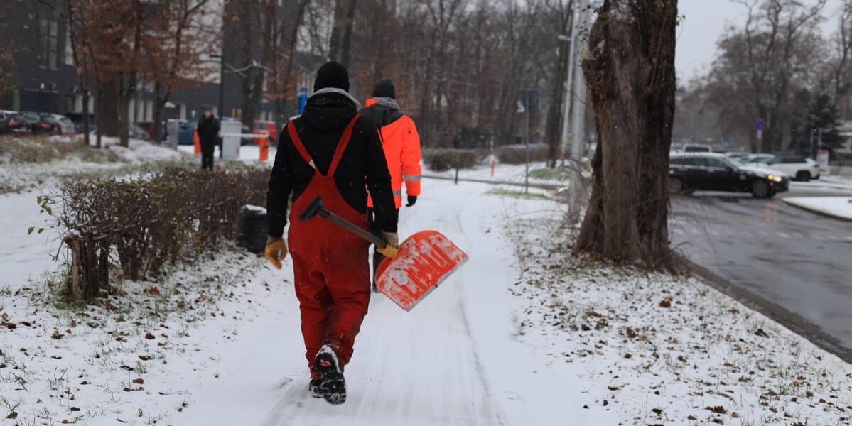 Pierwszy śnieg tej zimy spadł we Wrocławiu w niedzielę wieczorem. Na zdjęciu widać mężczyznę niosącego zaśnieżonym chodnikiem szuflę do zgarniania śniegu.