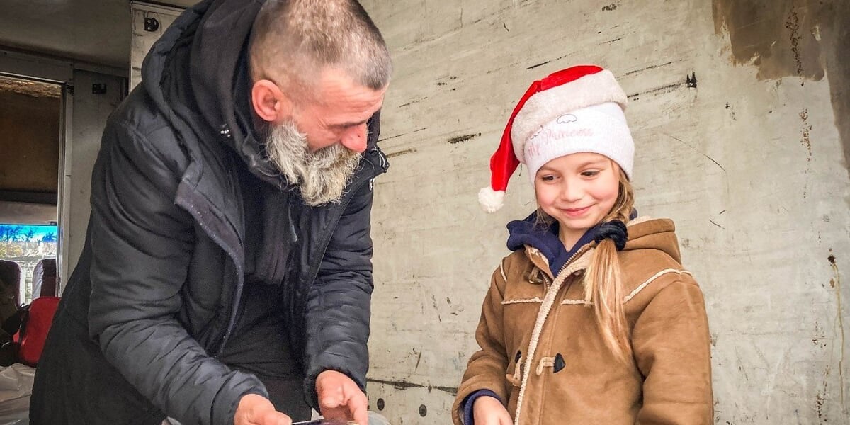 Mikołaj z Kramatorska. Donbas, grudzień 2022. Na zdjęciu starszy mężczyzna z małą dziewczynką.