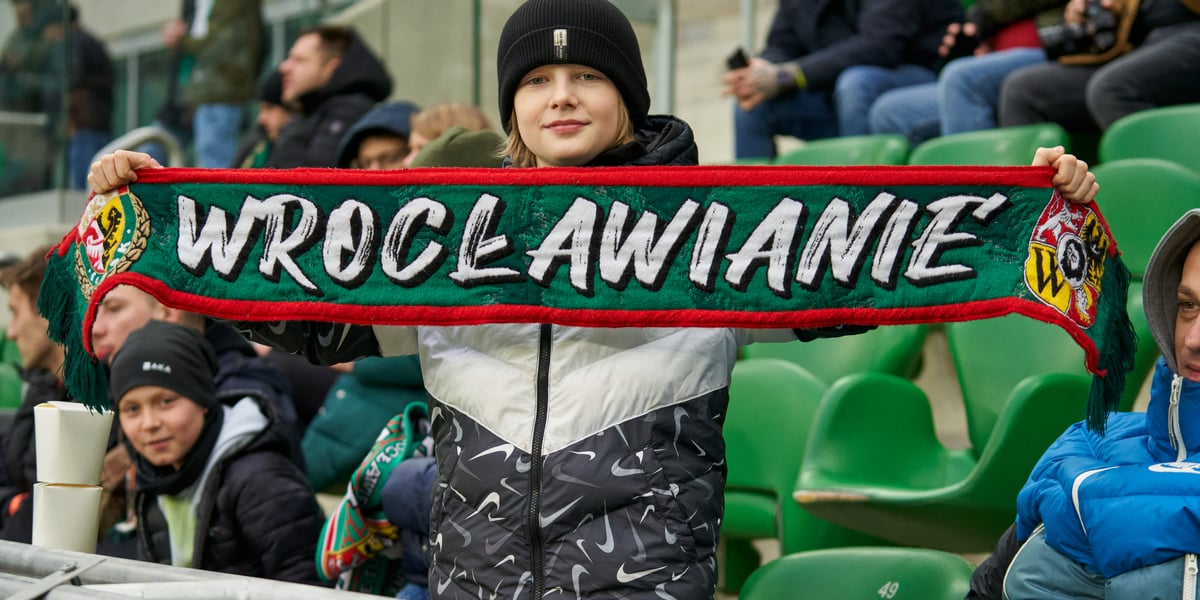 Na zdjęciu widać kibica na stadionie Tarczyński Arena na wrocławskich Pilczycach. W rękach trzyma szalik z napisem "Wrocławianie" 