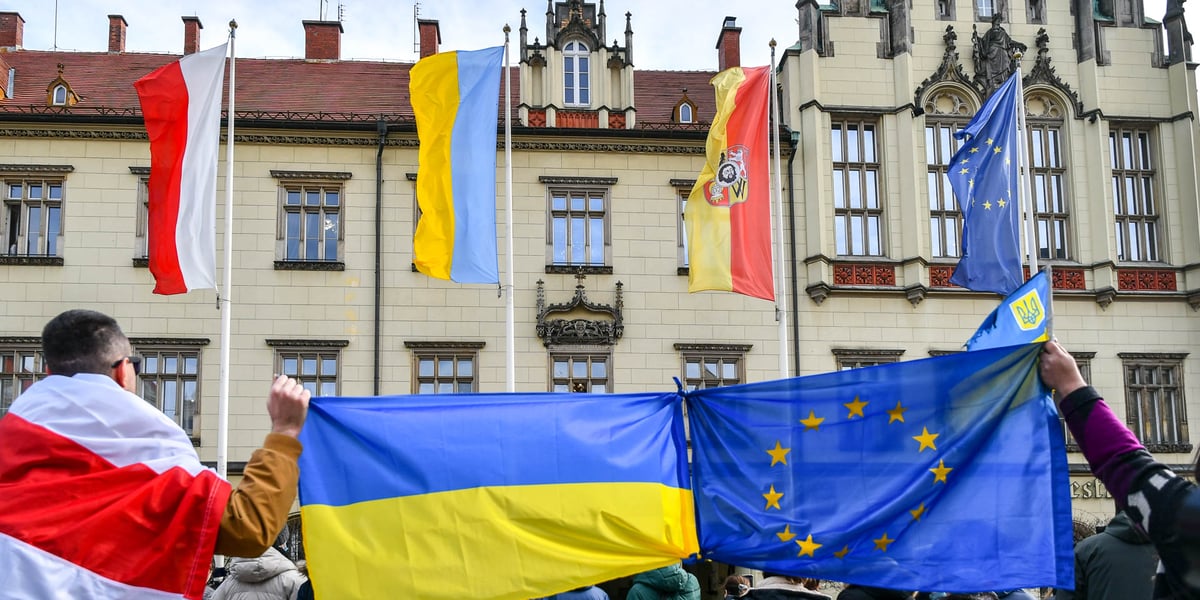 Na zdjęciu flagi wiszące przed wrocławskim ratuszem: polska, ukraińska, wrocławska i Unii Europejskiej. Na pierwszym planie dwie osoby trzymają związane ze sobą rogami flagi Ukrainy i Unii Europejskiej. Zdjęcie ilustracyjne.