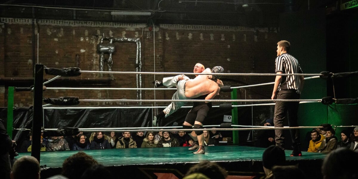 Na zdjęciu dwóch zawodników walczących w ringu podczas zawodów Maniac Zone Wrestling w zajezdni Dąbie. W narożniku ringu stoi sędzia. Wrocław 11.03.2023
