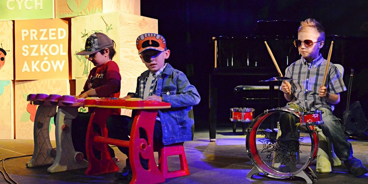 Trzech przedszkolaków na scenie. Chłopiec z prawej strony gra na miniaturowej perkusji, dwaj chłopcy z lewej na kolorowych keyboardach. Zdjęcie ilustracyjne z jednej z poprzednich Edycji Festiwalu Śpiewających Przedszkolaków.