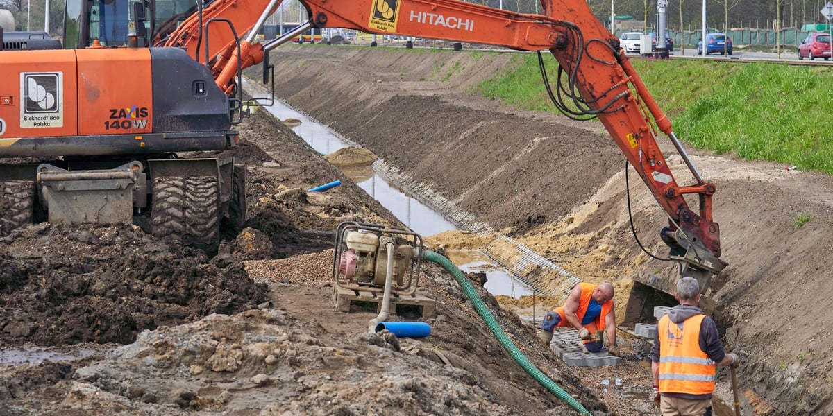 Ramię koparki nad rowem i dwójka mężczyzn na placu przebudowy ulicy Kosmonautów