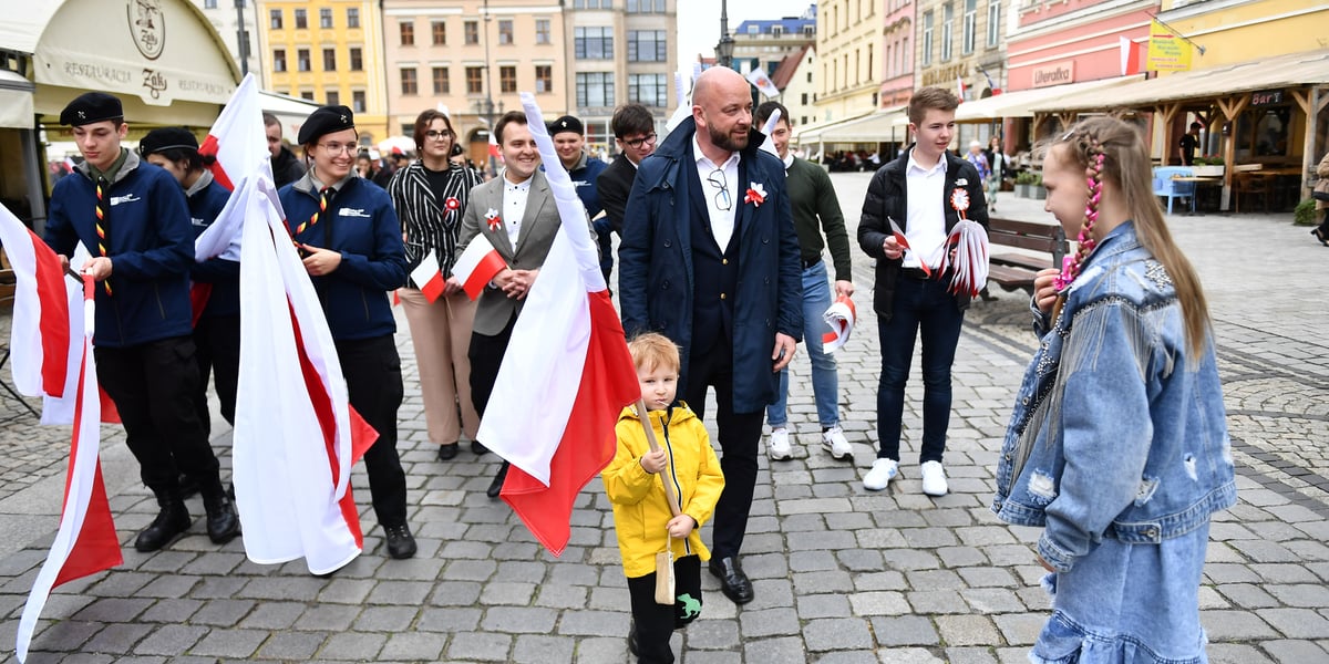Prezydent Jacek Sutryk rozdaje flagi. Młodzież radośnie przejmuje biało-czerwoną. 