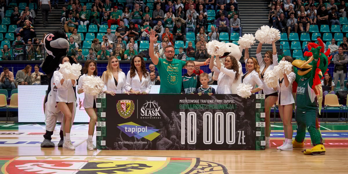 Kibic, czirliderki i maskotki na środku boiska z symbolicznym czekiem na 10 000 zł