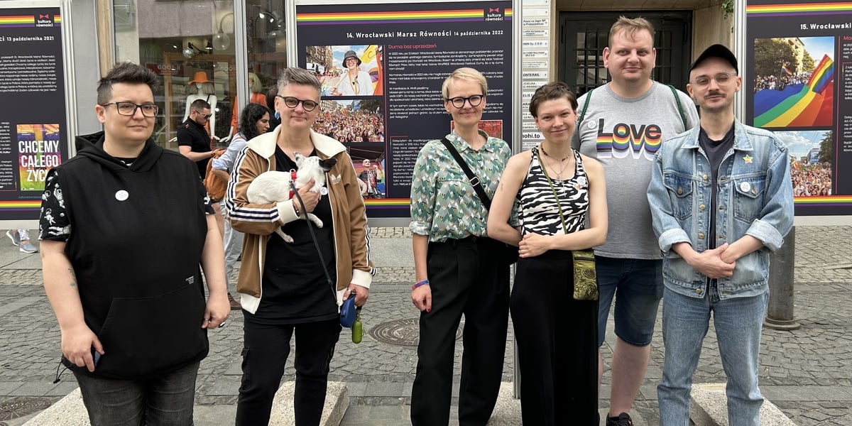 Ludzie na tle wystawy „15 lat Wrocławskich Marszów Równości” na ulicy Oławskiej