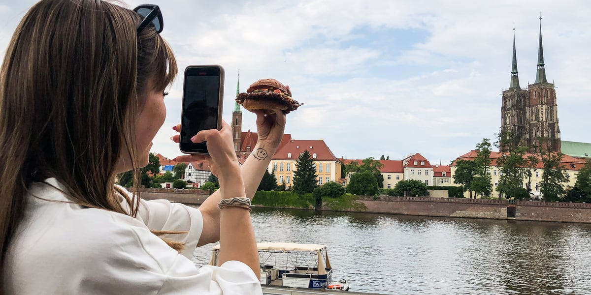 Kobieta na tle Ostrowa Tumskiego fotografuje burgera kupionego podczas Gastro Miasto 