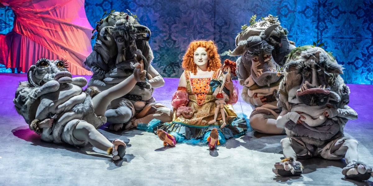 Scena ze spektaklu w Teatrze Lalek, na środku sceny siedzi rudowłosa Ojeja w kolorowej sukience, otaczają ją inni bohaterowie 