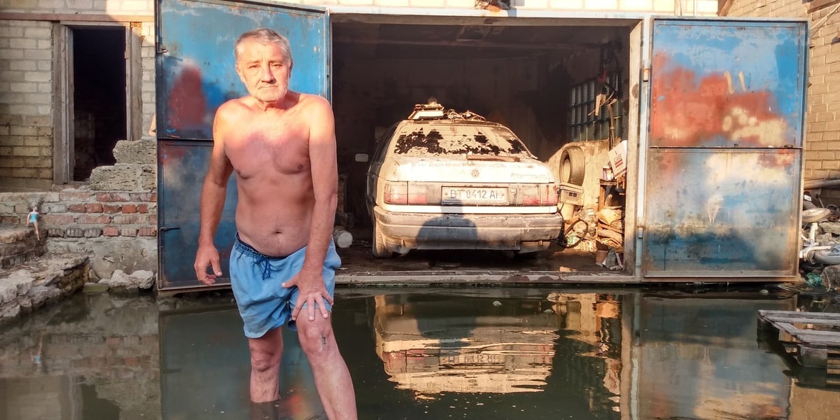 Wasilij z Chersonia stoi na podwórku swojego domu zalanego przez Dniepr. W tle w garażu jego samochód, który po powodzi nadaje się tylko na złom