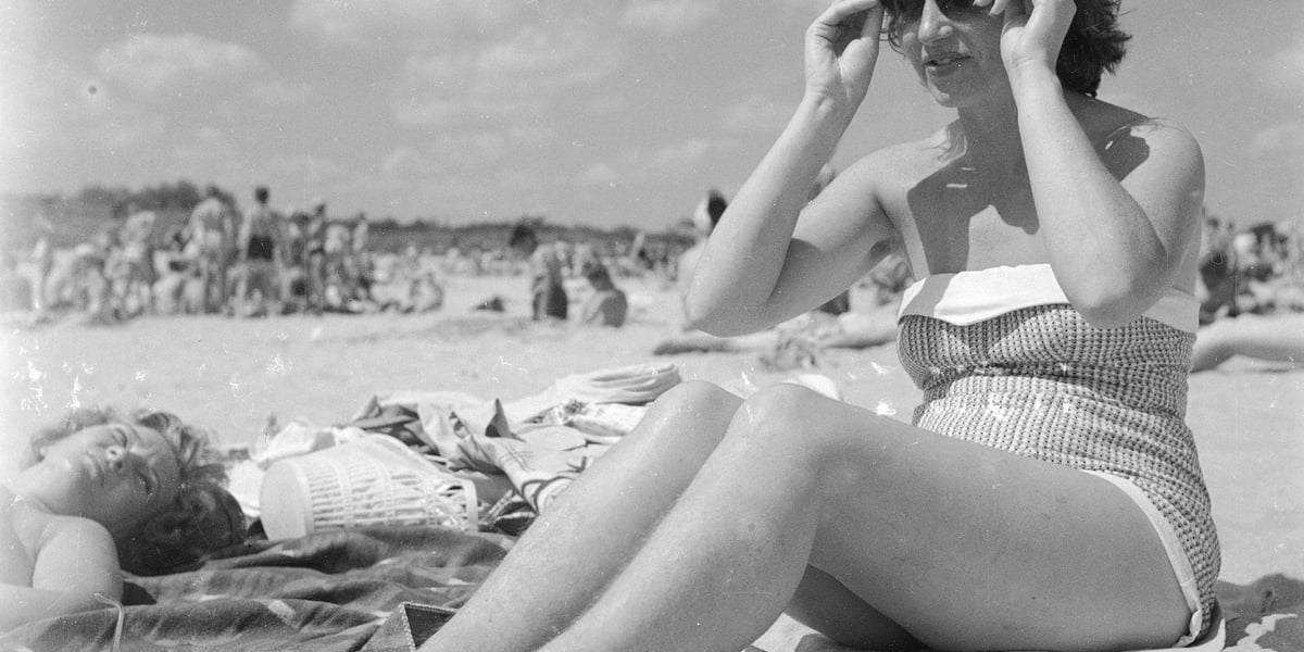 Wakacje nad Bałtykiem w PRL-u. Młoda kobieta siedzi na plaży w kostiumie kąpielowym i okularach. Rok 1958