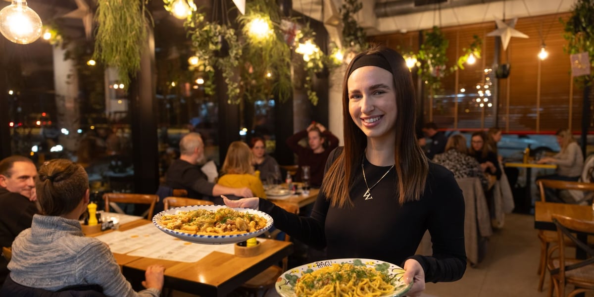 Uśmiechnięta kelnerka z potrawami na talerzach w Ragu Pracownia Makaronu