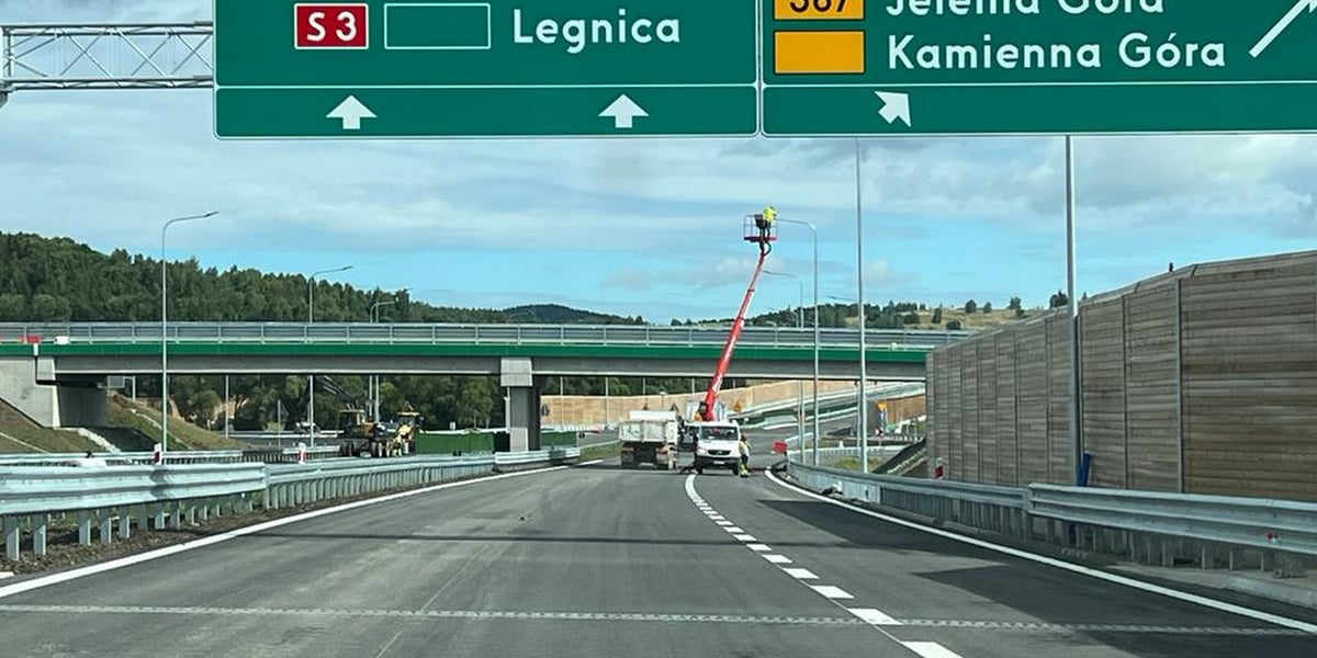 Ulica, a nad nią zielone tablice z napisami. Na jednej: S3 Legnica, na drugiej: Jelenia Góra, Kamienna Góra  