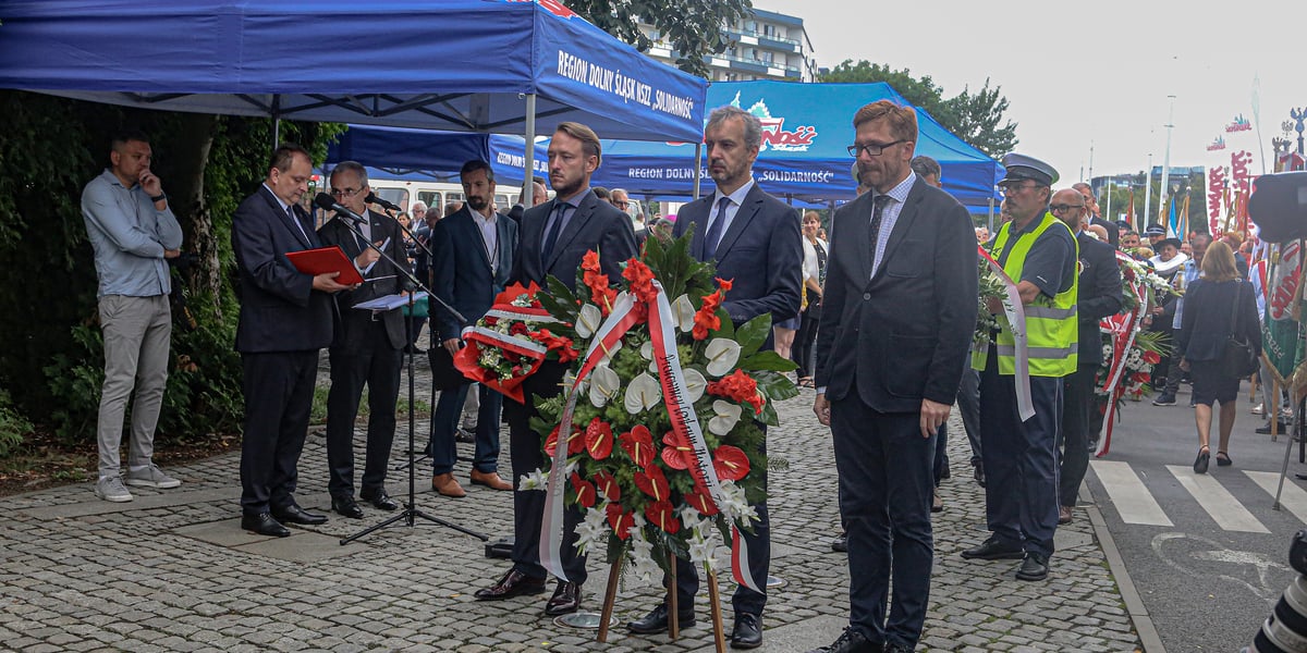 Obchody 43. rocznicy powstania NSZZ „Solidarność”. Mężczyźni składają kwiaty pod tablicą Solidarności