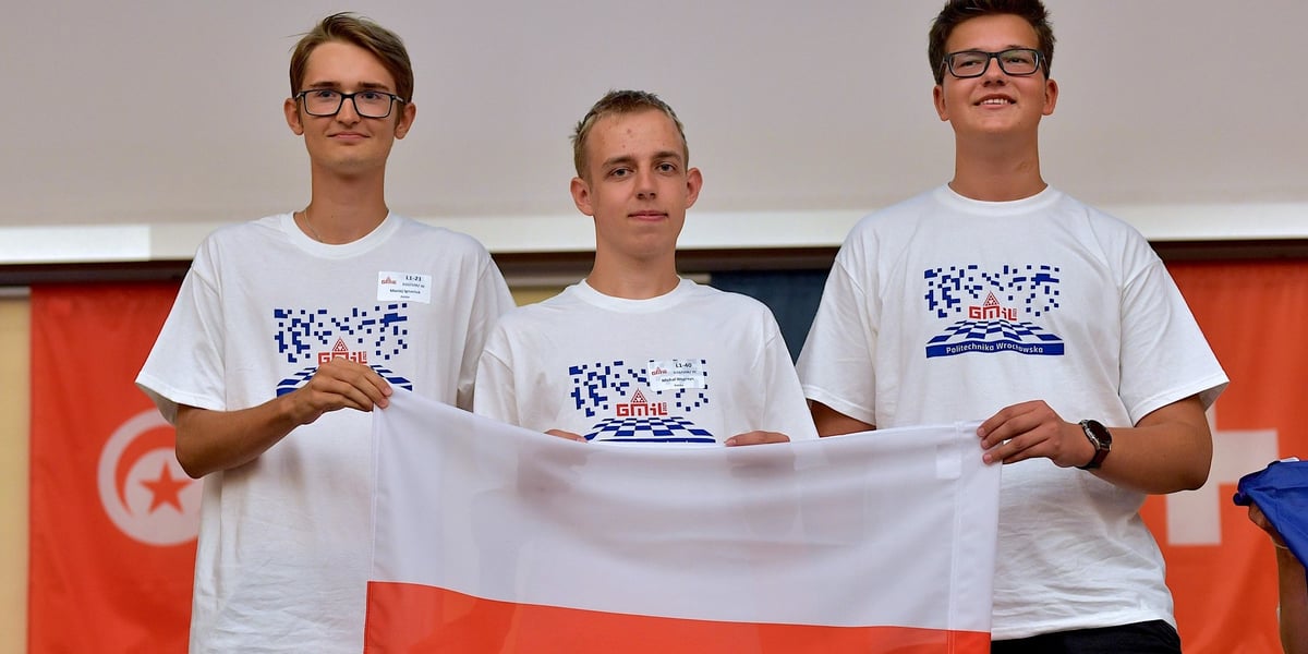 Trzech chłopców, którzy przed sobą trzymają rozpostartą flagę Polki