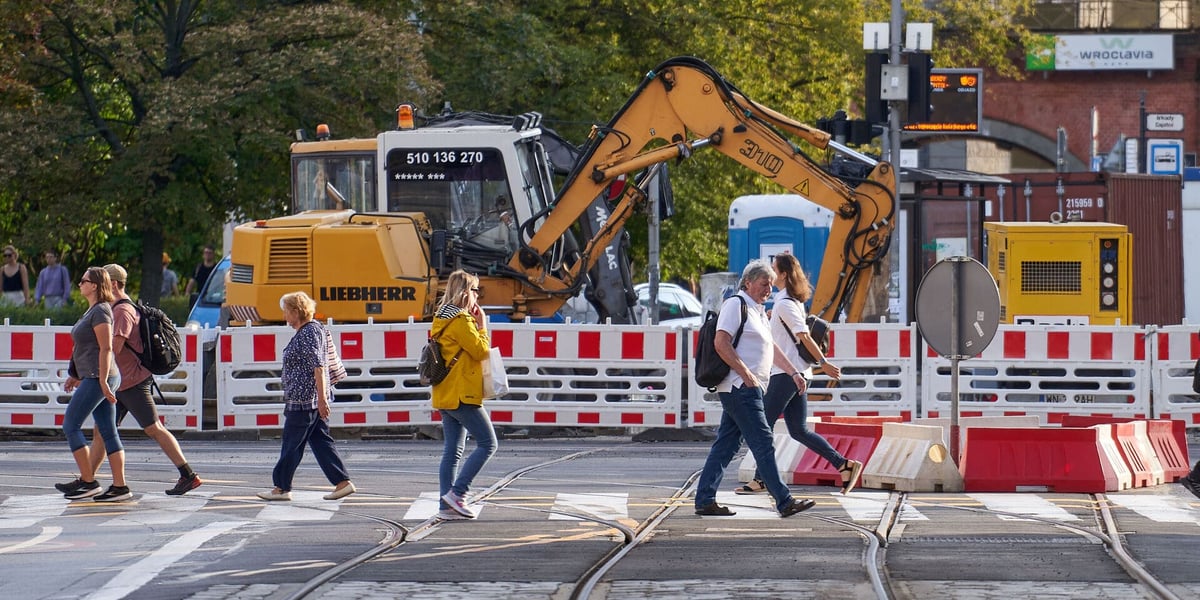 Przechodnie na przejściu dla pieszych. W tle koparka i plac budowy związany z remontem torowiska na skrzyżowaniu ulic Piłsudskiego i Świdnickiej we Wrocławiu.